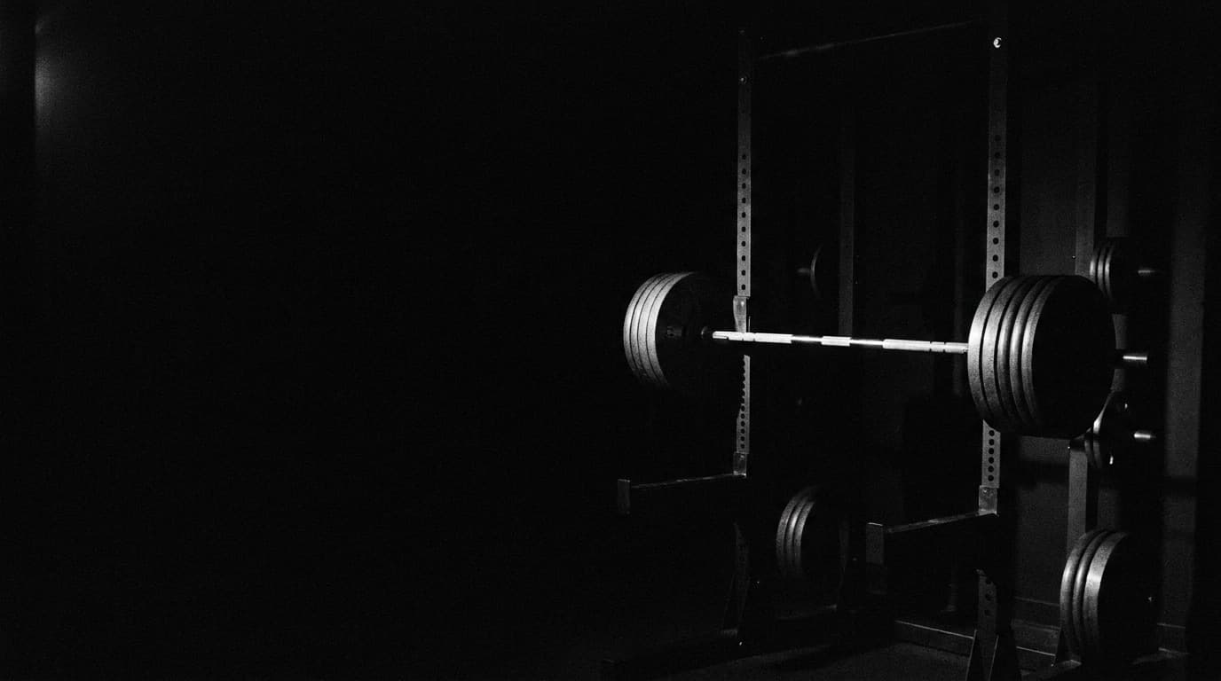 a loaded barbell resting on a power rack in a dark, empty gym